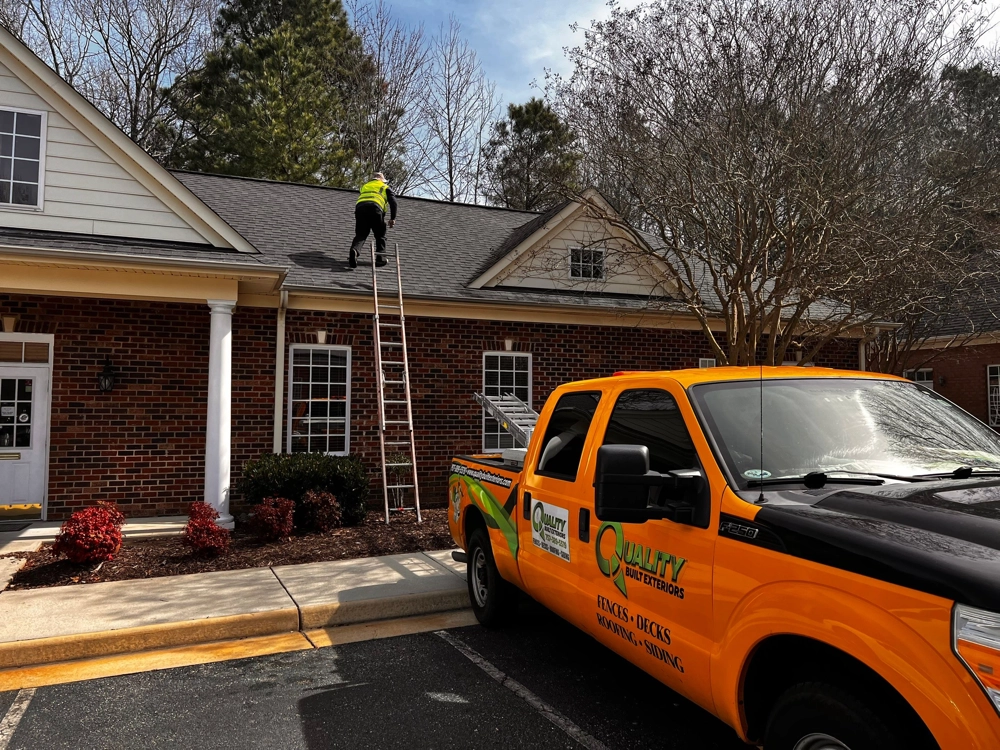 Roofer working on top of house with with QBX Truck in front