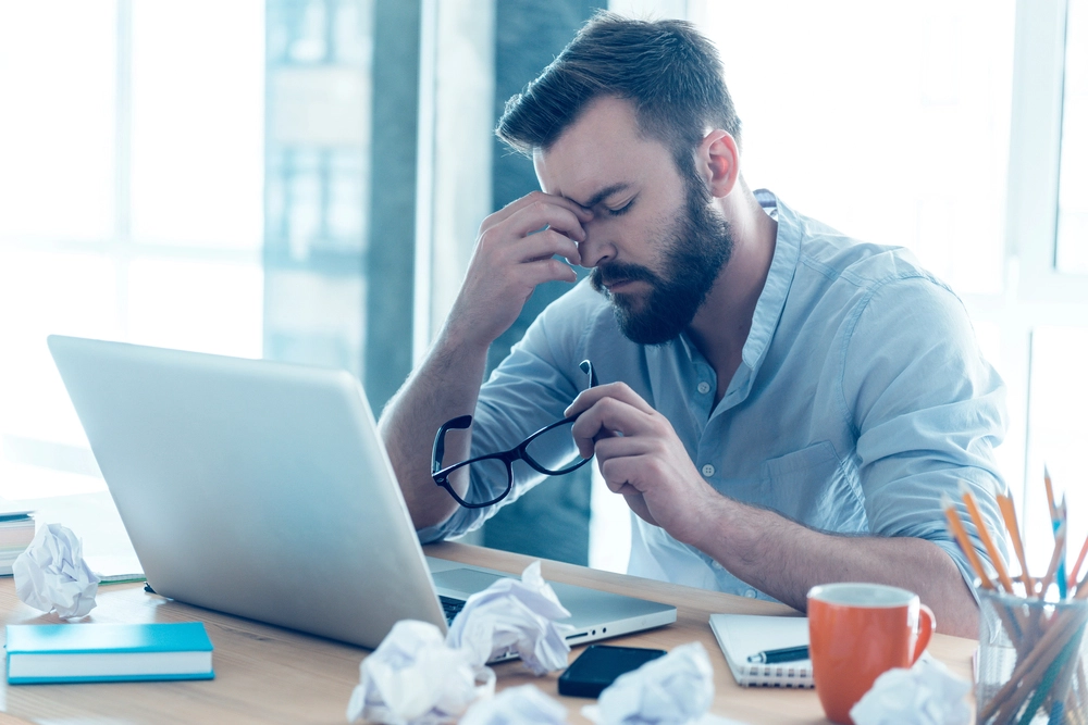 frustrated man sitting in front of computer holding eye glasses